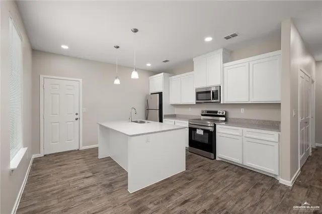 a kitchen with stainless steel appliances granite countertop a stove top oven a sink a refrigerator white cabinets and wooden floor