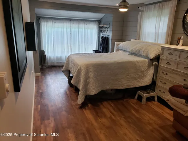 a bedroom with a bed a dresser and potted plants with wooden floor