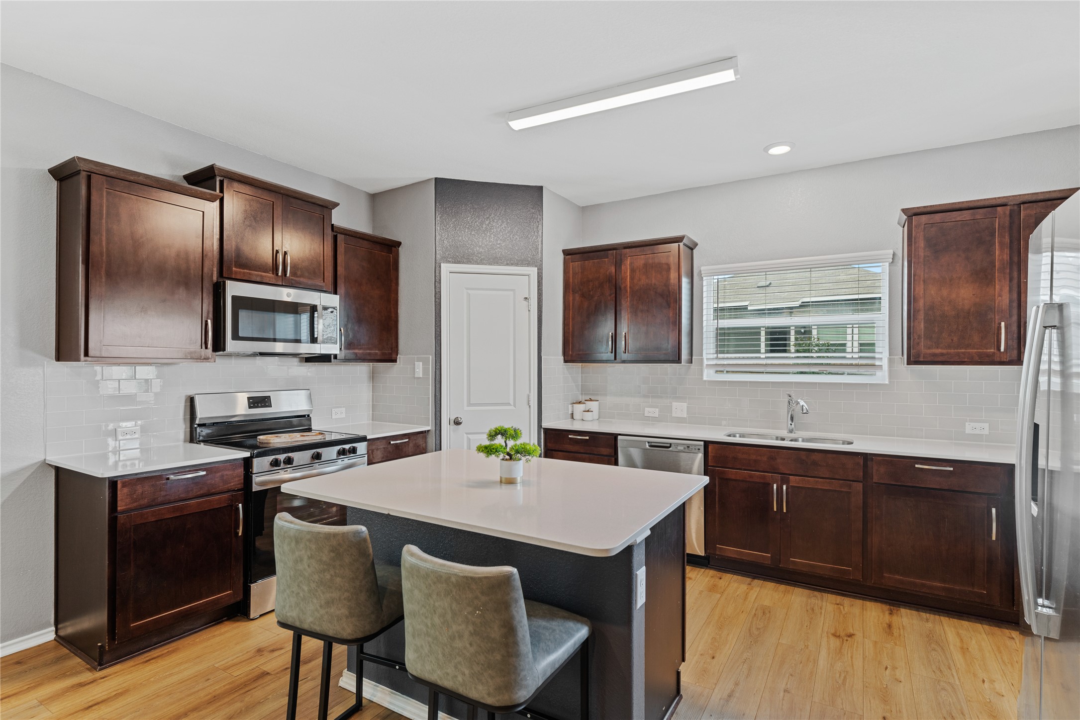 425 Perfect World Loop Jarrell, TX 76537 - Photo 8 of 29 Modern kitchen featuring rich wood-finish cabinetry, light countertops, and a subway tile backsplash