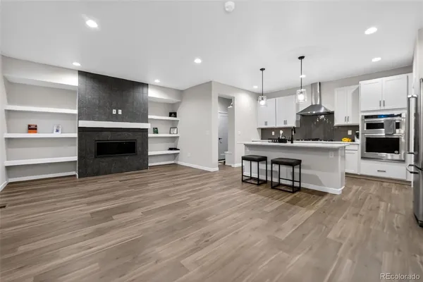 a open kitchen with kitchen island a stove a refrigerator and a fireplace with wooden floor