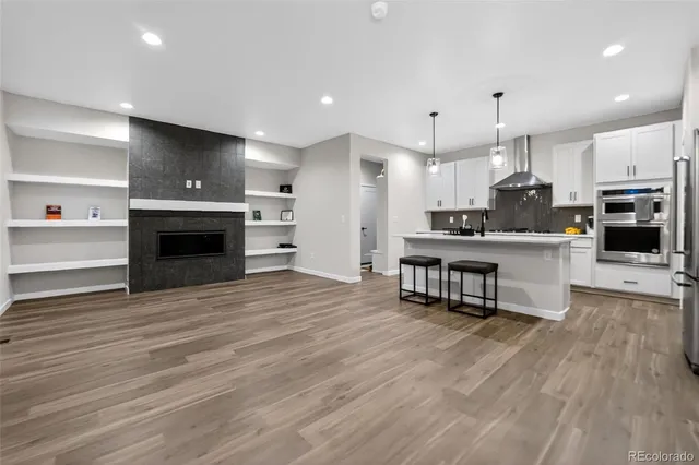 a open kitchen with kitchen island a stove a refrigerator and a fireplace with wooden floor