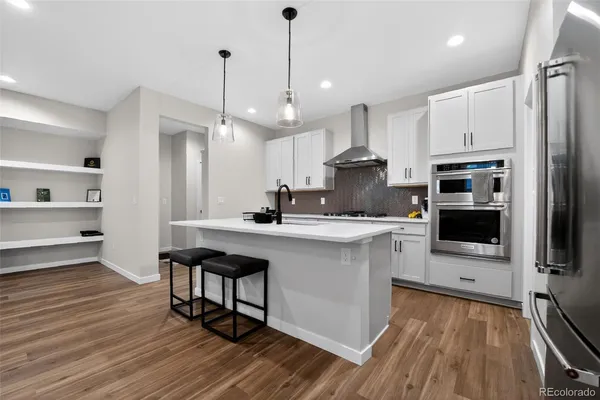 a kitchen with stainless steel appliances a stove a sink dishwasher a refrigerator and white cabinets with wooden floor