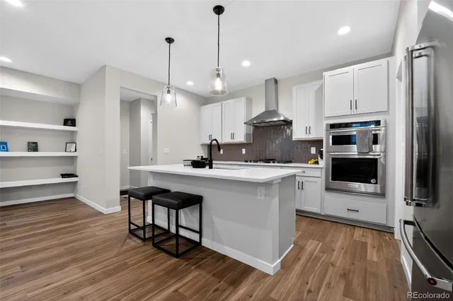 a kitchen with stainless steel appliances a stove a sink dishwasher a refrigerator and white cabinets with wooden floor