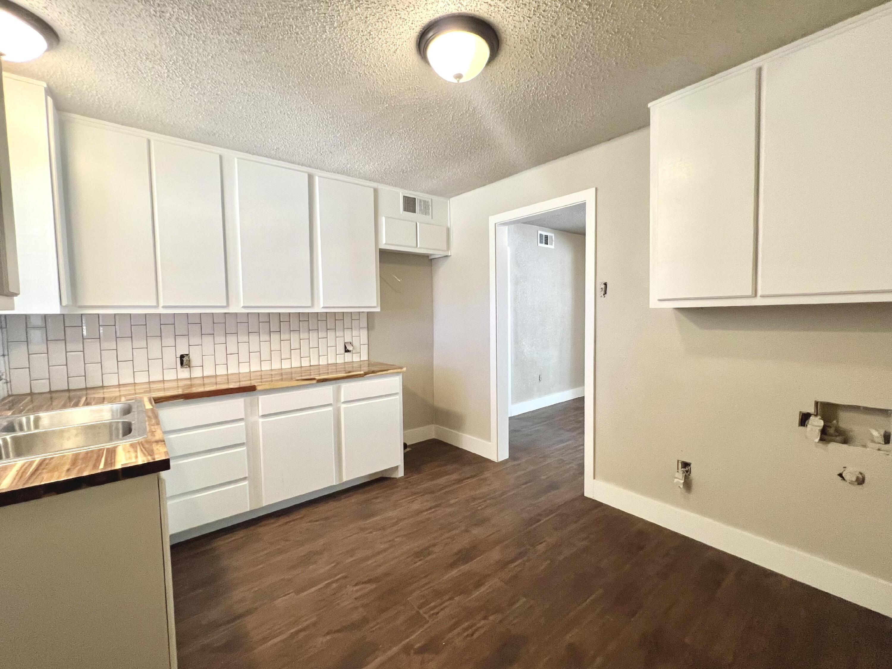 2620 25th Street Lubbock, TX 79410 - Photo 7 of 16 a large kitchen with a refrigerator a sink dishwasher and white cabinets with wooden floor