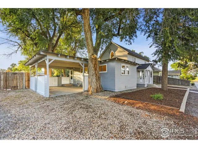 a view of a white house with a large tree and wooden fence