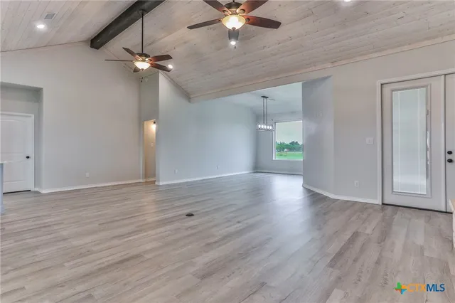 a view of an empty room with wooden floor and a ceiling fan