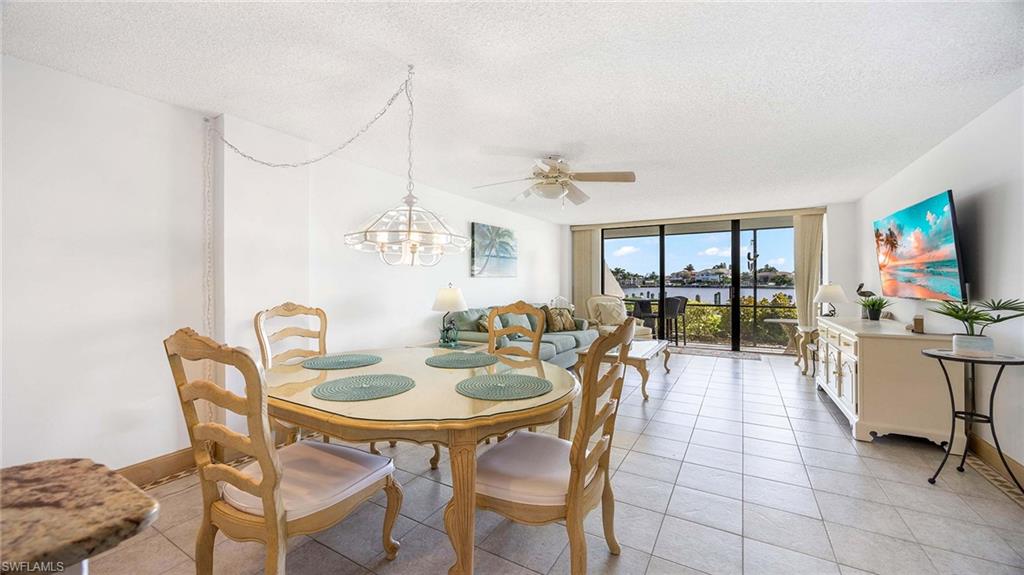 601 Seaview Court, Unit C106 Marco Island, FL 34145 - Photo 6 of 42 Dining space featuring floor to ceiling windows, a textured ceiling, a ceiling fan, light tile patterned flooring, and a chandelier