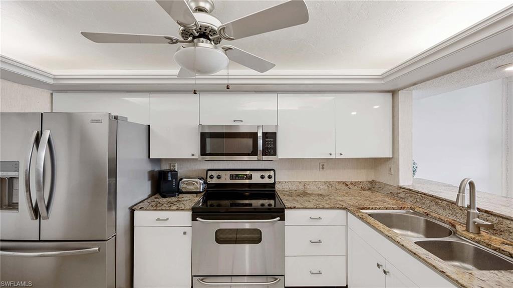 601 Seaview Court, Unit C106 Marco Island, FL 34145 - Photo 9 of 42 Kitchen with stainless steel appliances, light stone counters, white cabinets, and a ceiling fan