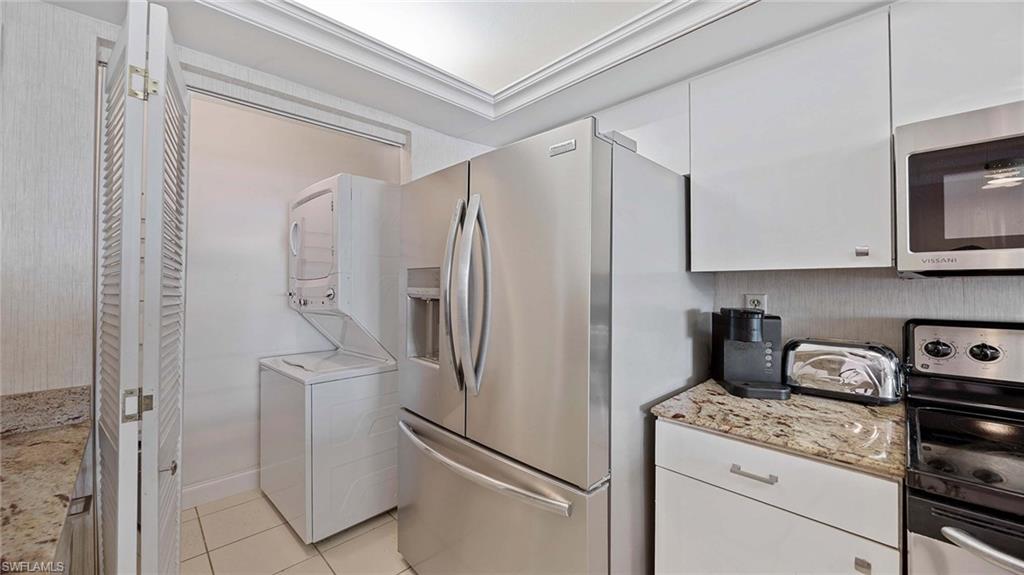 601 Seaview Court, Unit C106 Marco Island, FL 34145 - Photo 10 of 42 Kitchen with appliances with stainless steel finishes, white cabinetry, light stone countertops, light tile patterned flooring, and stacked washing machine and dryer