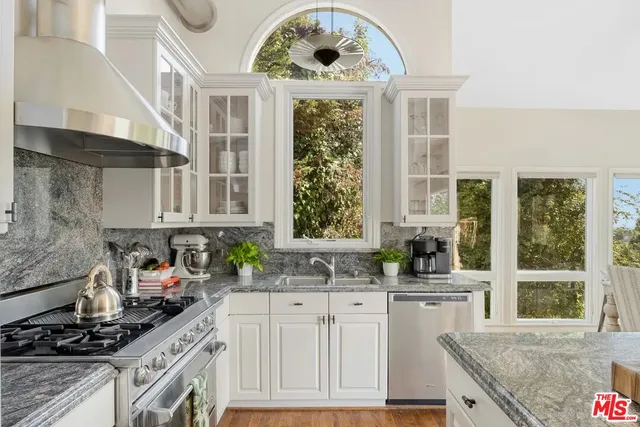 a kitchen with stainless steel appliances granite countertop a stove top oven a sink dishwasher and a refrigerator with wooden floor