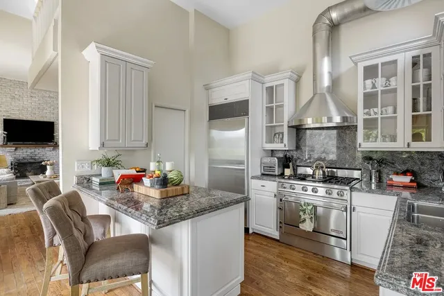 a kitchen with granite countertop a stove a sink and white cabinets with wooden floor