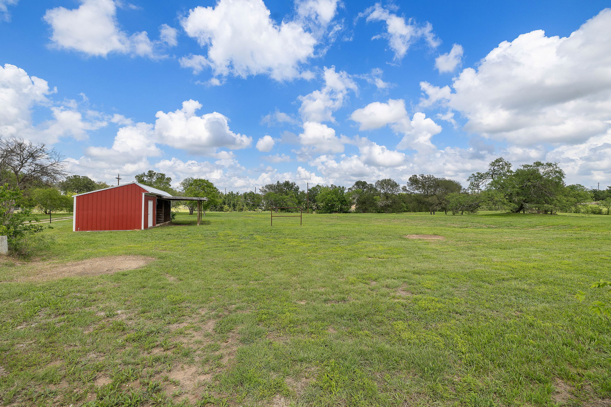 571 Balch Road Elgin, TX 78621 - Photo 31 of 33 Red metal barn with a covered lean-to structure, set within a spacious grassy field