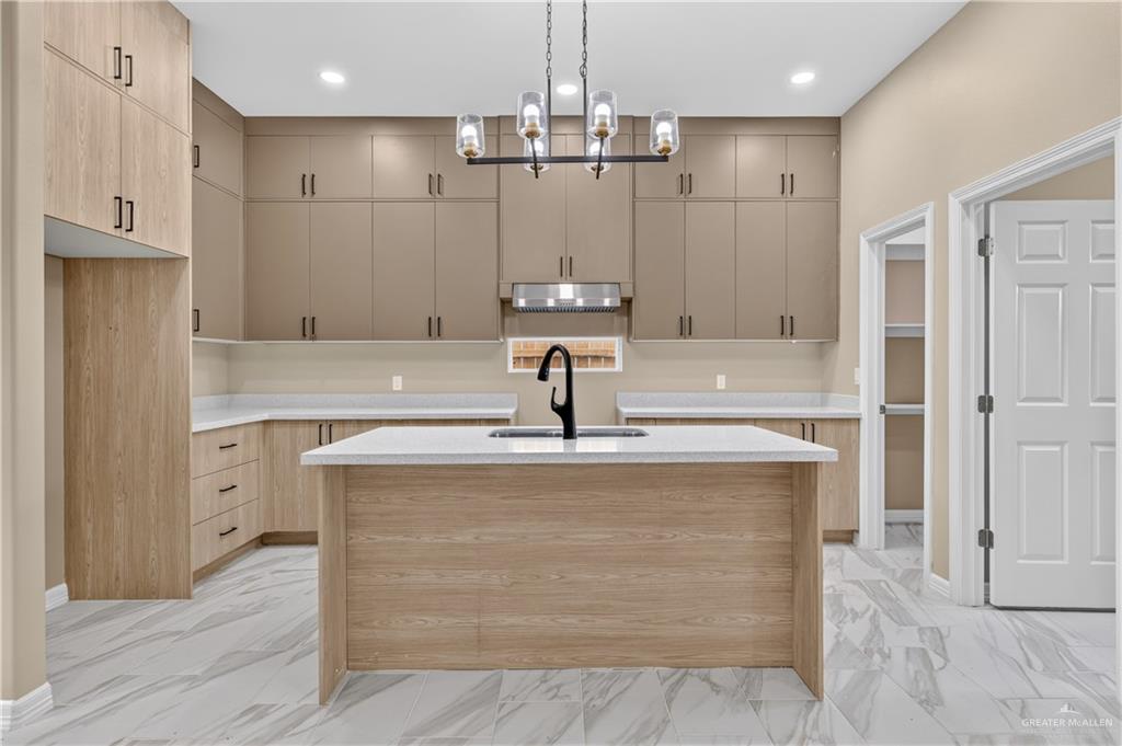 1920 Trinity Street Donna, TX 78537 - Photo 8 of 23 Contemporary kitchen featuring a central island, light wood-finish cabinetry, gray upper cabinetry, light-toned countertops, and a modern chandelier