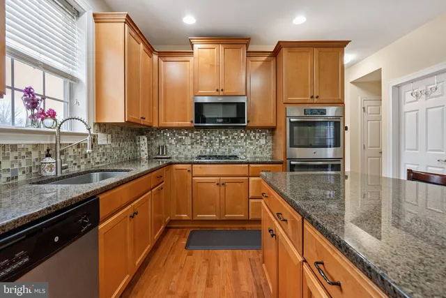 a kitchen with stainless steel appliances granite countertop a refrigerator a stove a sink a dining table and chairs with wooden floor