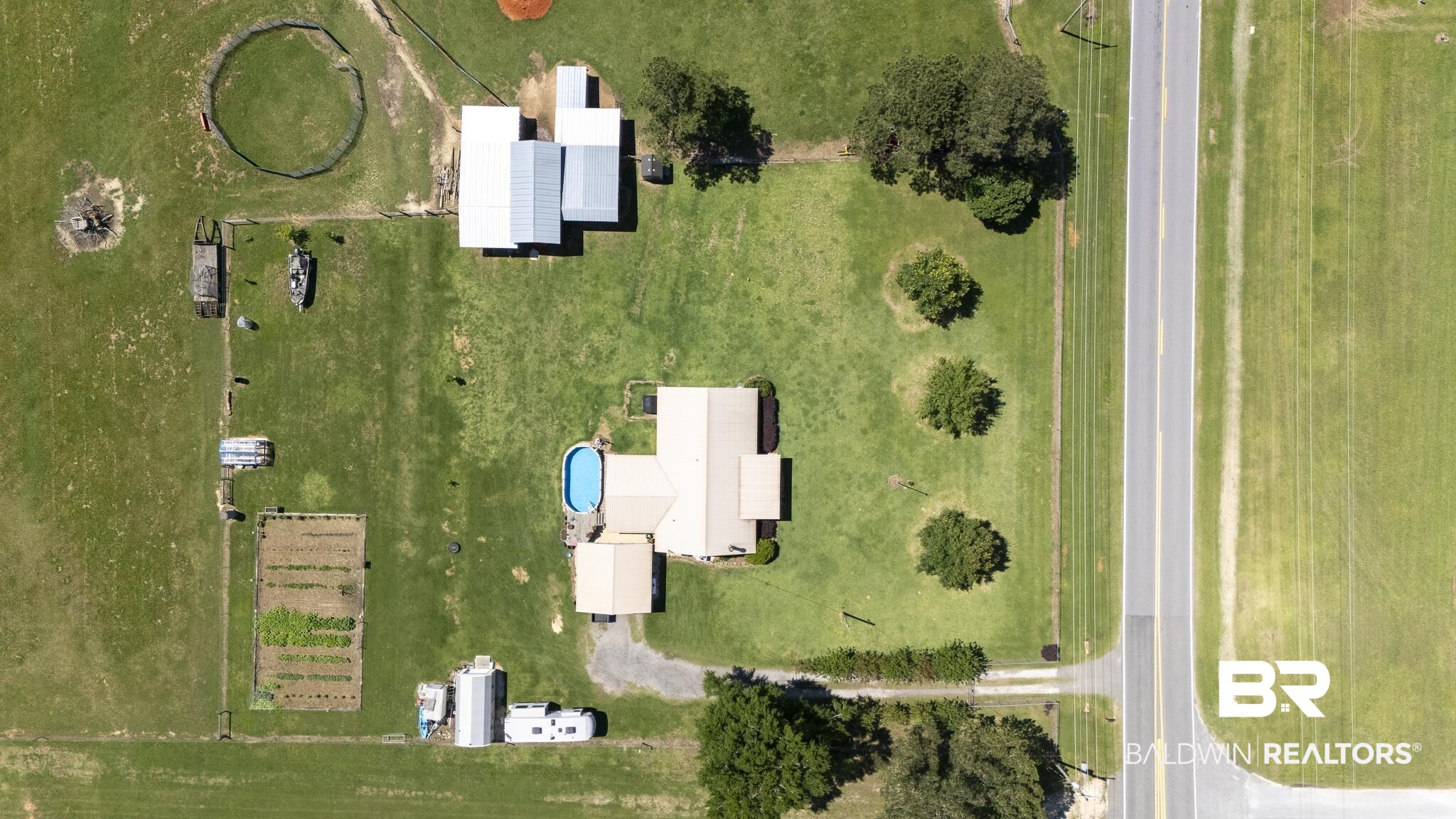 30580 County Road 49 Loxley, AL 36551 - Photo 19 of 32 Expansive property featuring a main residence, an oval-shaped pool, multiple outbuildings with metal roofs, a livestock corral, and a cultivated garden area