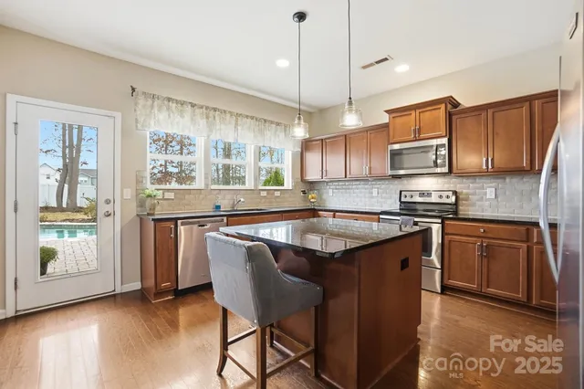 a kitchen with stainless steel appliances granite countertop a sink a stove a refrigerator a center island and a window