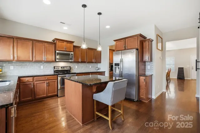 a kitchen with stainless steel appliances granite countertop a refrigerator a stove a sink dishwasher and a microwave with wooden floor