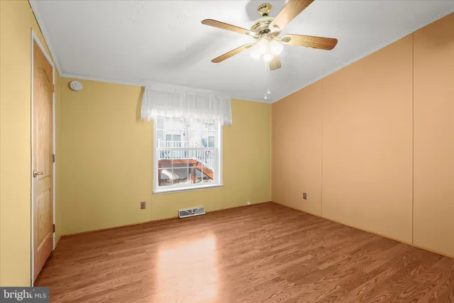 a view of an empty room with wooden floor and a ceiling fan