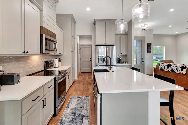 a large kitchen with stainless steel appliances a stove a sink dishwasher and a refrigerator with wooden floor