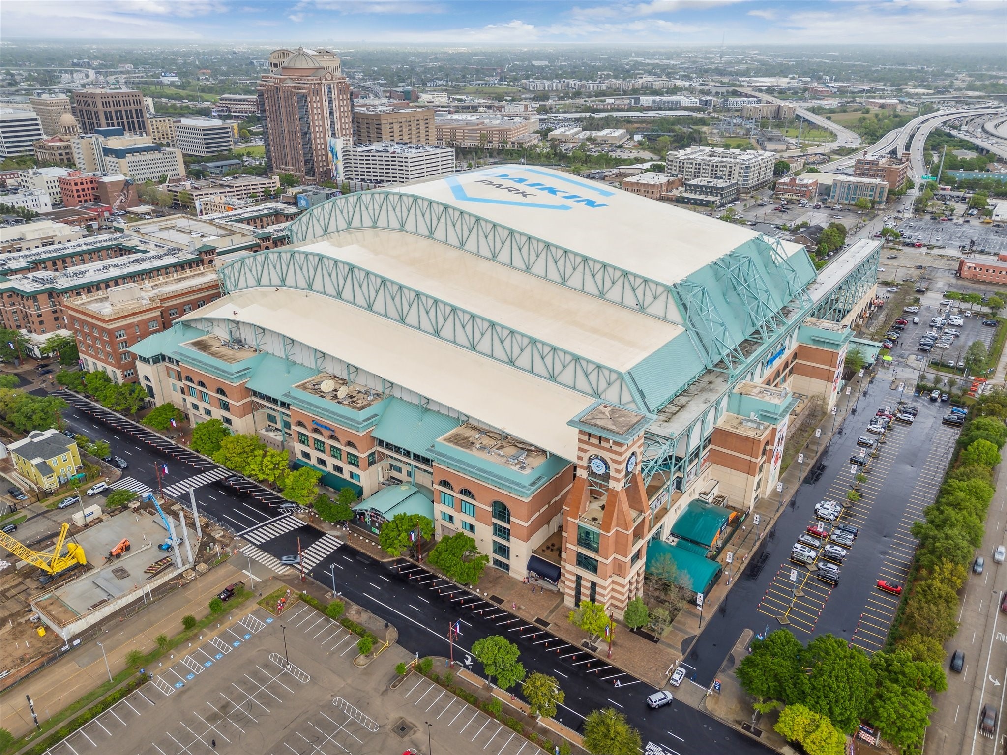 1111 Caroline Street, Unit 2908 Houston, TX 77010 - Photo 38 of 50 Soaring over downtown Houston, the photo captures Daikin Park, home of the Houston Astros, with its recognizable retractable roof and clock tower at the corner. Surrounding the ballpark, you can see a mix of modern office towers, historic brick buildings, and busy freeway interchanges stretching into the distance. The vibrant grid of city streets, parking areas, and tree-lined sidewalks emphasize its central location, while the open roofline stands out as a landmark in the skyline.
