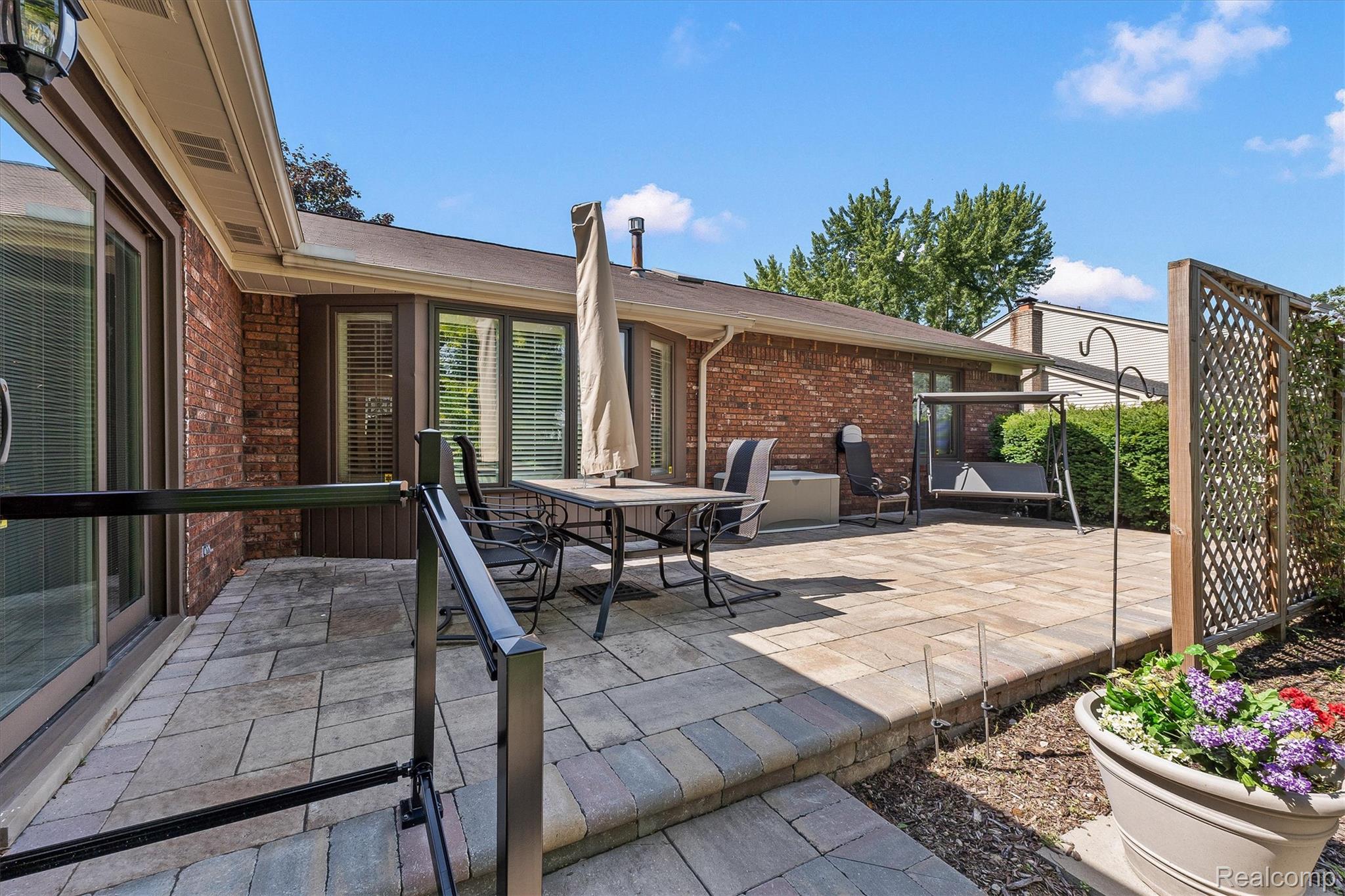1662 Sumac Drive Rochester, MI 48309 - Photo 34 of 38 Expansive paver patio with a tiered design, featuring brick exterior, sliding glass door access, and a decorative privacy screen