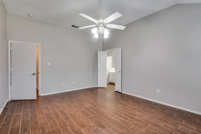 a view of an empty room with wooden floor and a ceiling fan