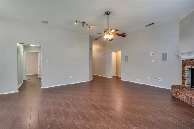 a view of an empty room with wooden floor and a ceiling fan