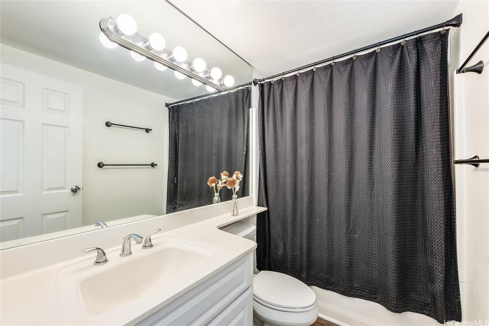 87-119 Helelua Street, Unit F202 Waianae, HI 96792 - Photo 12 of 25 a bathroom with a sink a toilet a mirror and shower curtain