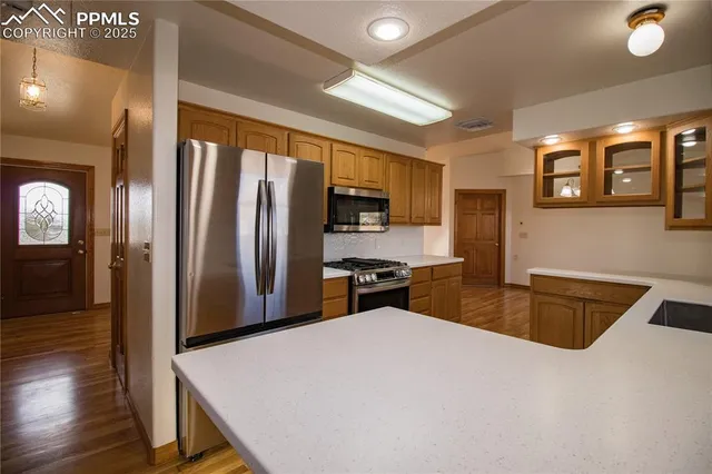 a kitchen with stainless steel appliances granite countertop a refrigerator a sink dishwasher a stove and white countertops with wooden floor