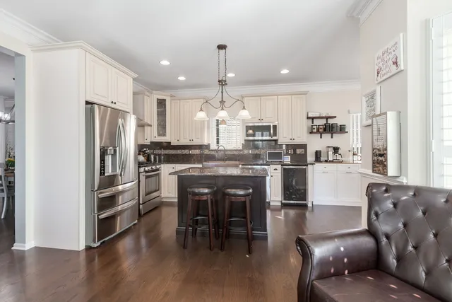 a kitchen with stainless steel appliances kitchen island granite countertop a refrigerator a stove a sink a dining table and chairs with wooden floor