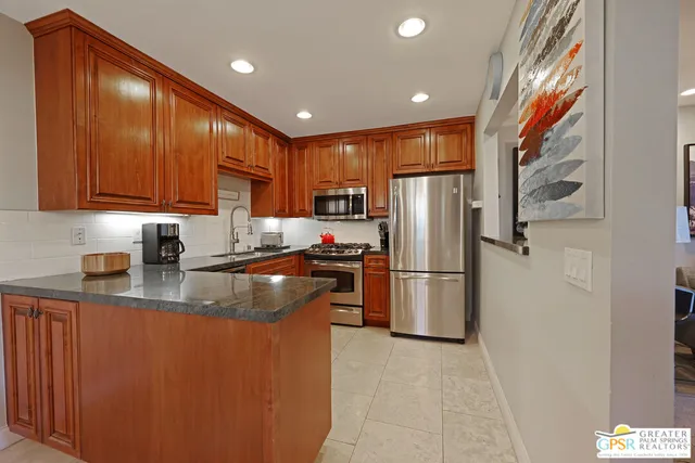 a kitchen with stainless steel appliances granite countertop a refrigerator a sink a stove a washer dryer and a refrigerator