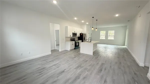 a living room with stainless steel appliances kitchen island granite countertop a refrigerator a stove top oven a sink and dishwasher with wooden floor