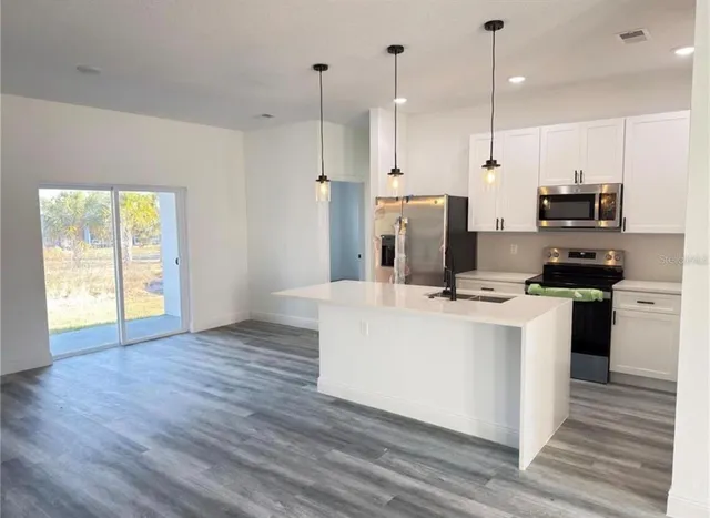 a kitchen with stainless steel appliances a stove a sink a refrigerator a center island with wooden floor