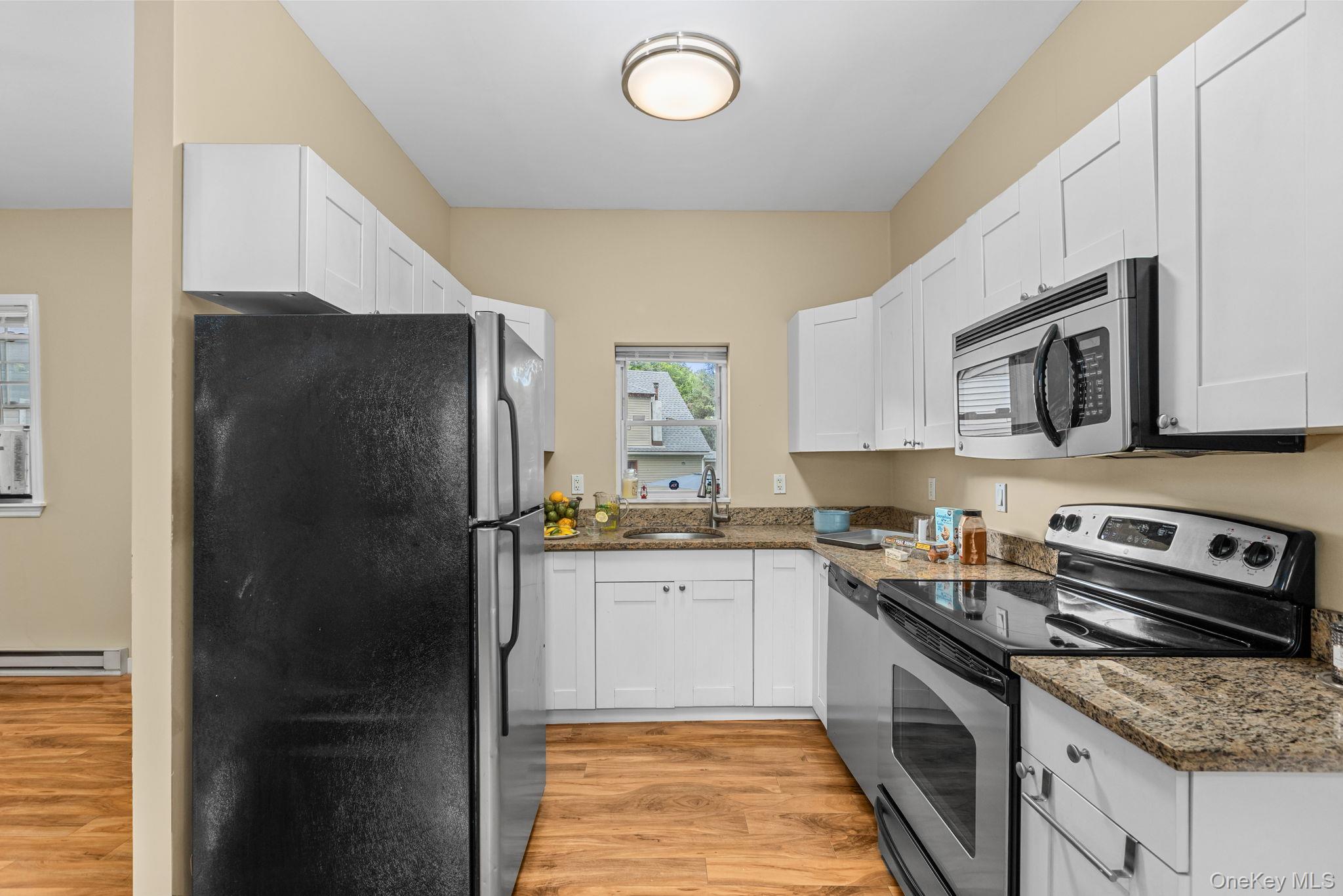 10 Batavia Road Patterson, NY 12563 - Photo 13 of 42 Galley kitchen featuring white soft-close cabinetry, wood-finish flooring, stainless steel appliances, granite-style countertops, and a ceiling-mounted light fixture.