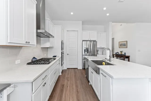 a kitchen with stainless steel appliances a stove a sink a refrigerator and white cabinets