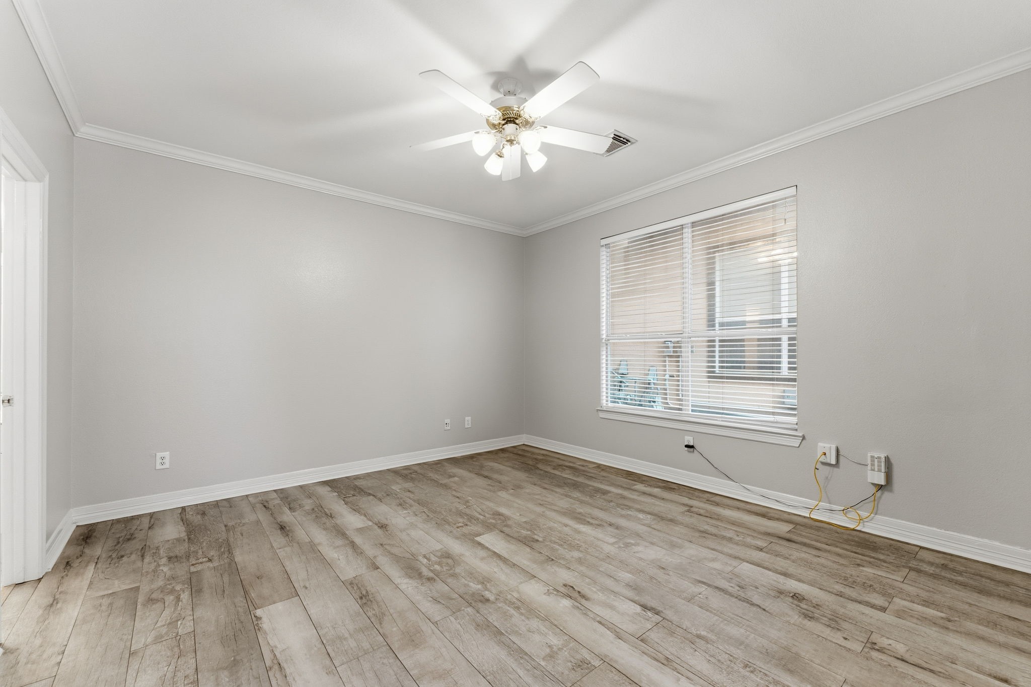 827 Rosine Street Houston, TX 77019 - Photo 11 of 50 This room features neutral gray walls and wood-look flooring, creating a modern and clean aesthetic. It is well-lit with a ceiling fan light fixture and a large window, providing ample natural light.