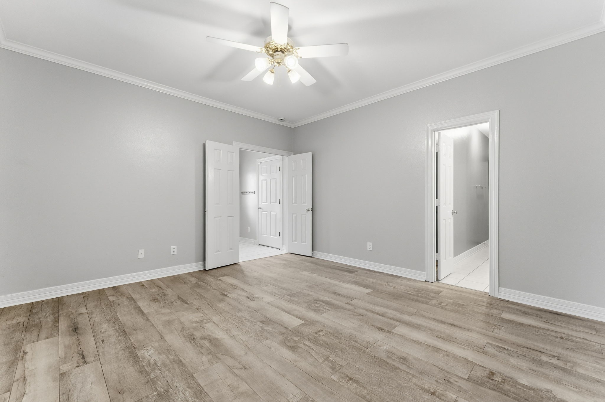 827 Rosine Street Houston, TX 77019 - Photo 12 of 50 Spacious bedroom with light gray walls and wood-look flooring, featuring a ceiling fan and ample natural light. It includes two doorways leading to a bathroom and additional space for versatility.