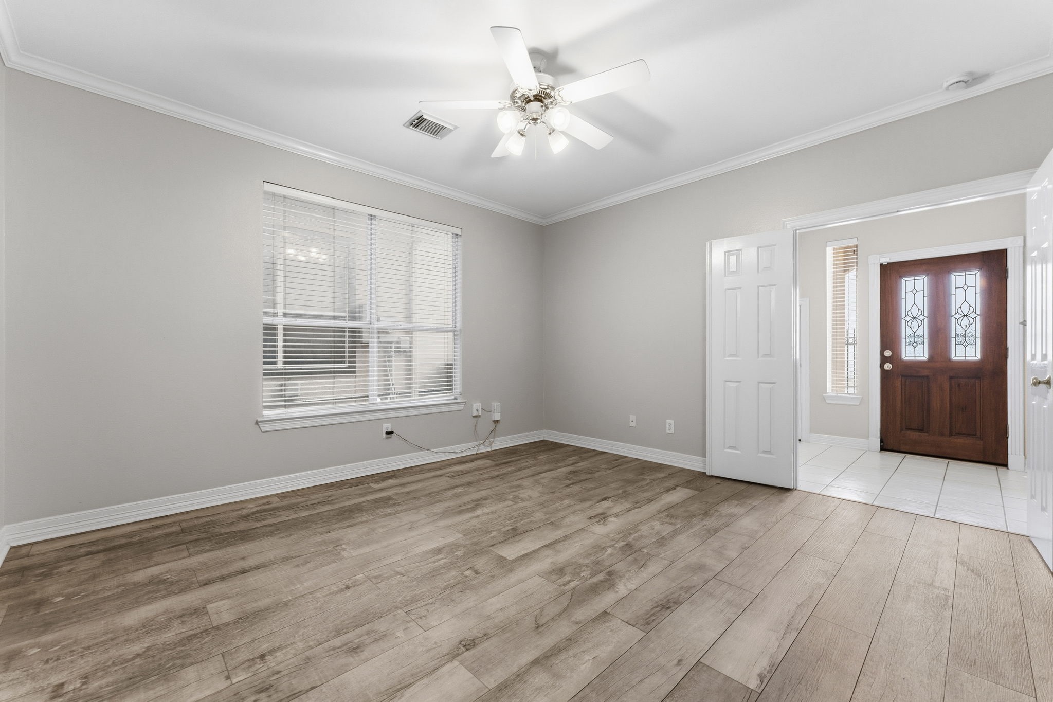 827 Rosine Street Houston, TX 77019 - Photo 13 of 50 This room features light wood flooring, neutral walls, and a ceiling fan. It has a large window for natural light and opens to a tiled entryway with a decorative wooden front door, creating a welcoming atmosphere.