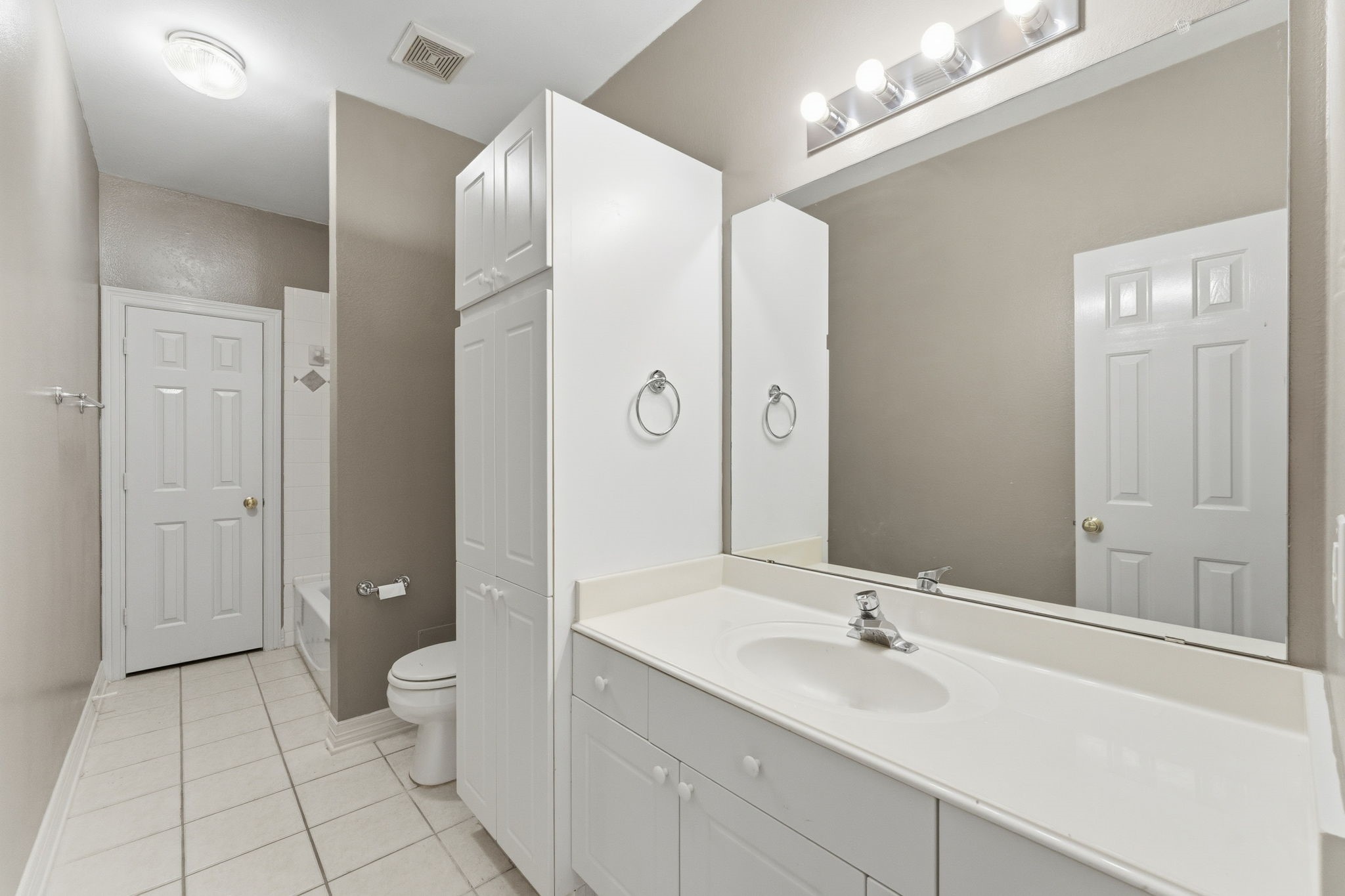 827 Rosine Street Houston, TX 77019 - Photo 14 of 50 This bathroom features a clean, modern design with neutral walls, white cabinetry, and tile flooring. It includes a large mirror, ample storage, and a well-lit vanity area, along with a bathtub and toilet.