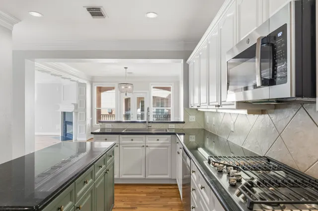 a kitchen with stainless steel appliances kitchen island granite countertop a refrigerator a stove a sink and white cabinets with wooden floor