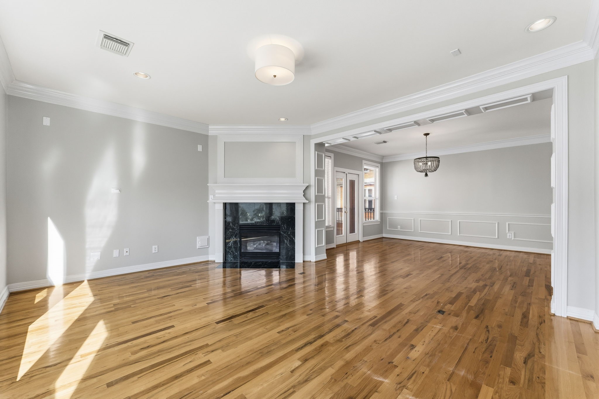 827 Rosine Street Houston, TX 77019 - Photo 22 of 50 This spacious living area features polished hardwood floors, a cozy fireplace, and elegant crown molding. An open layout leads into a bright dining room with a statement chandelier, perfect for entertaining.