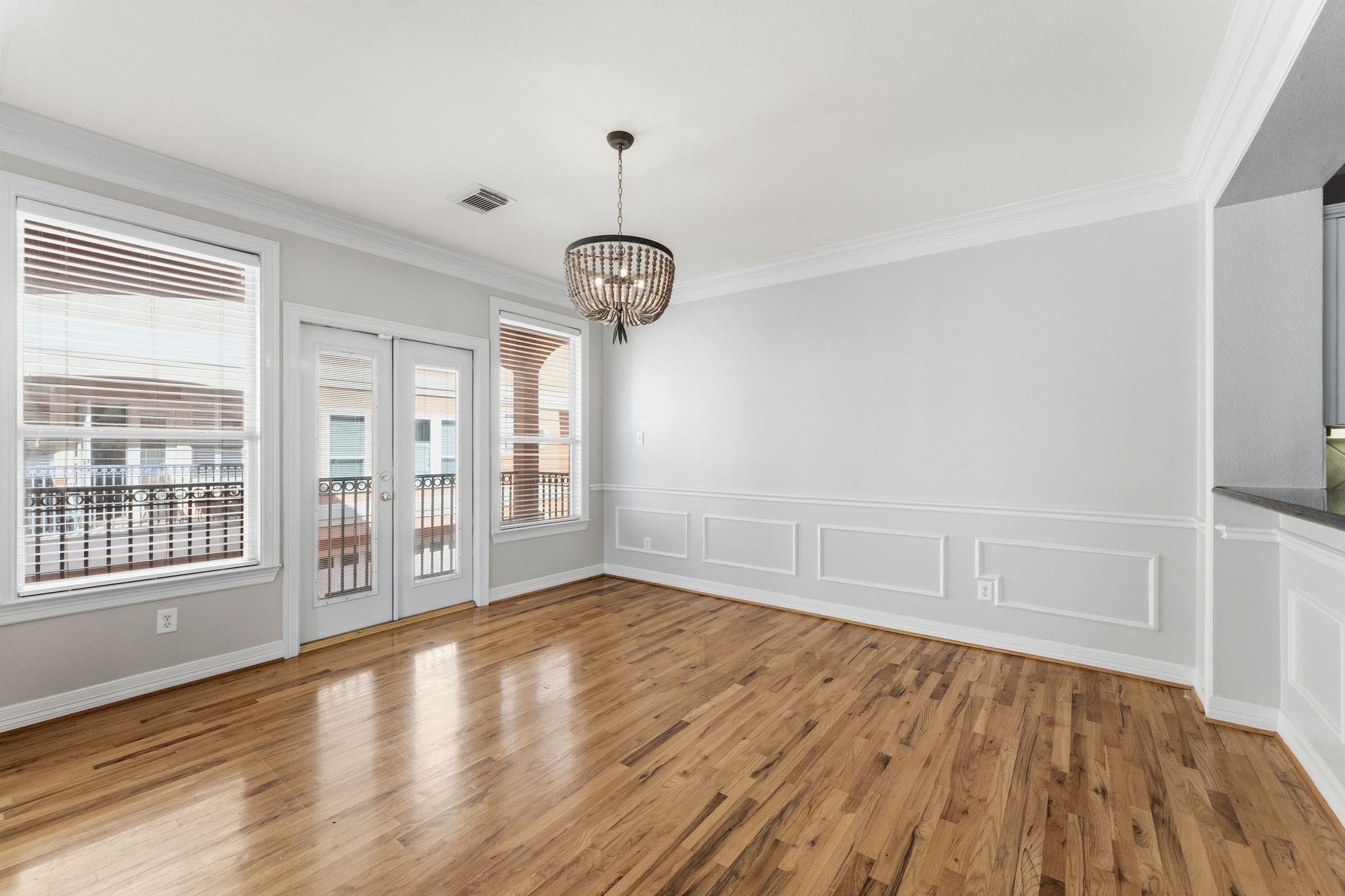 827 Rosine Street Houston, TX 77019 - Photo 24 of 50 Bright and spacious dining area with hardwood floors, elegant wainscoting, and large windows for natural light. Features French doors leading to a balcony. A stylish chandelier adds a touch of sophistication.