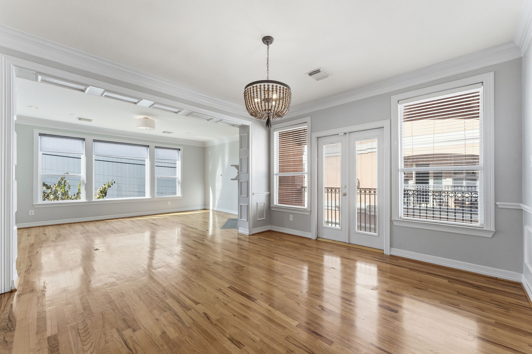 827 Rosine Street Houston, TX 77019 - Photo 25 of 50 This photo showcases a bright and spacious living area with hardwood floors, large windows, and French doors. The room is enhanced by elegant crown molding and a stylish chandelier, creating an inviting and open atmosphere.