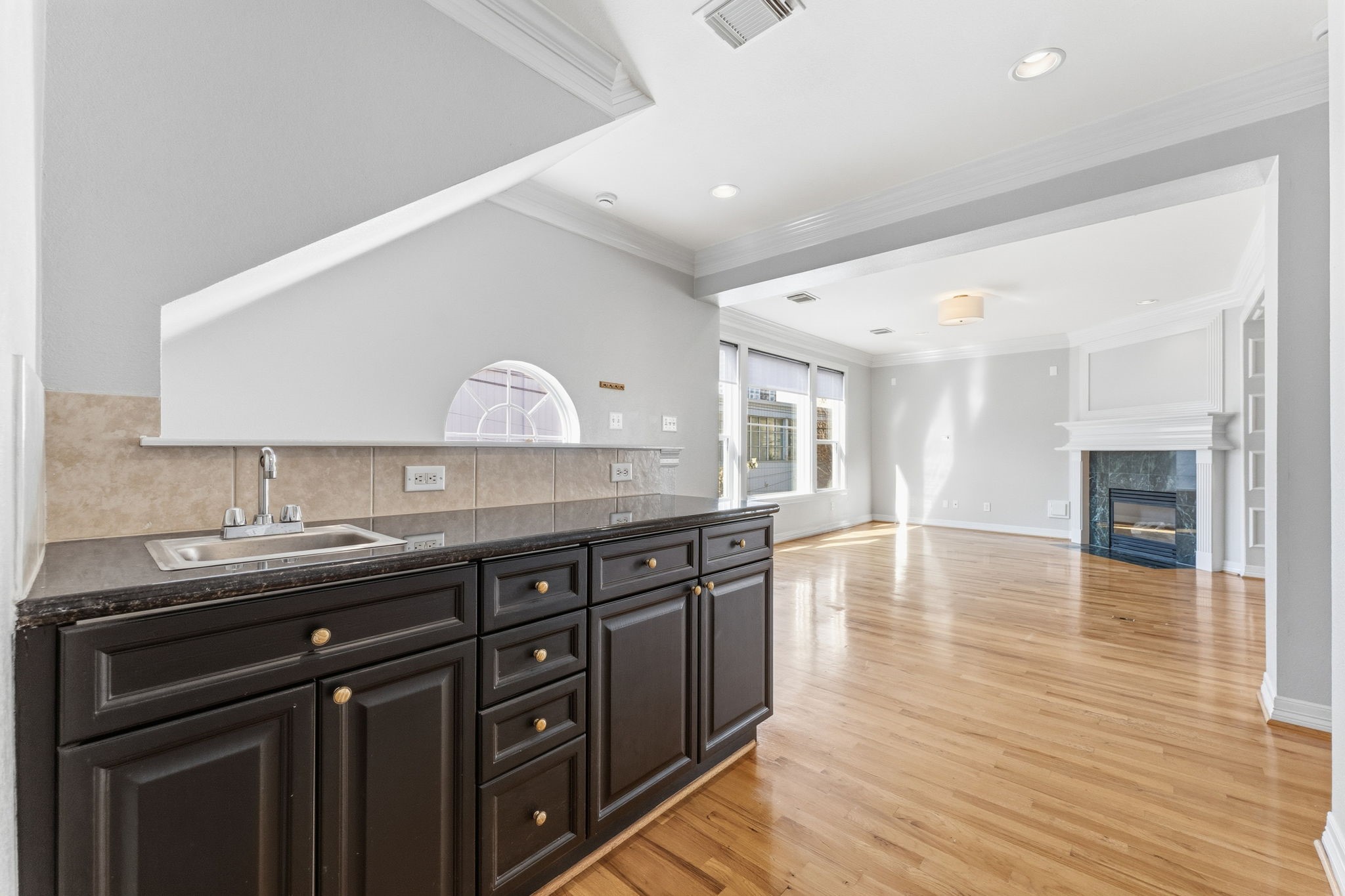 827 Rosine Street Houston, TX 77019 - Photo 32 of 50 This photo showcases a bright, open-concept living area featuring hardwood floors, a cozy fireplace, and a wet bar with dark cabinetry and granite countertops. Large windows provide plenty of natural light, creating a welcoming atmosphere.