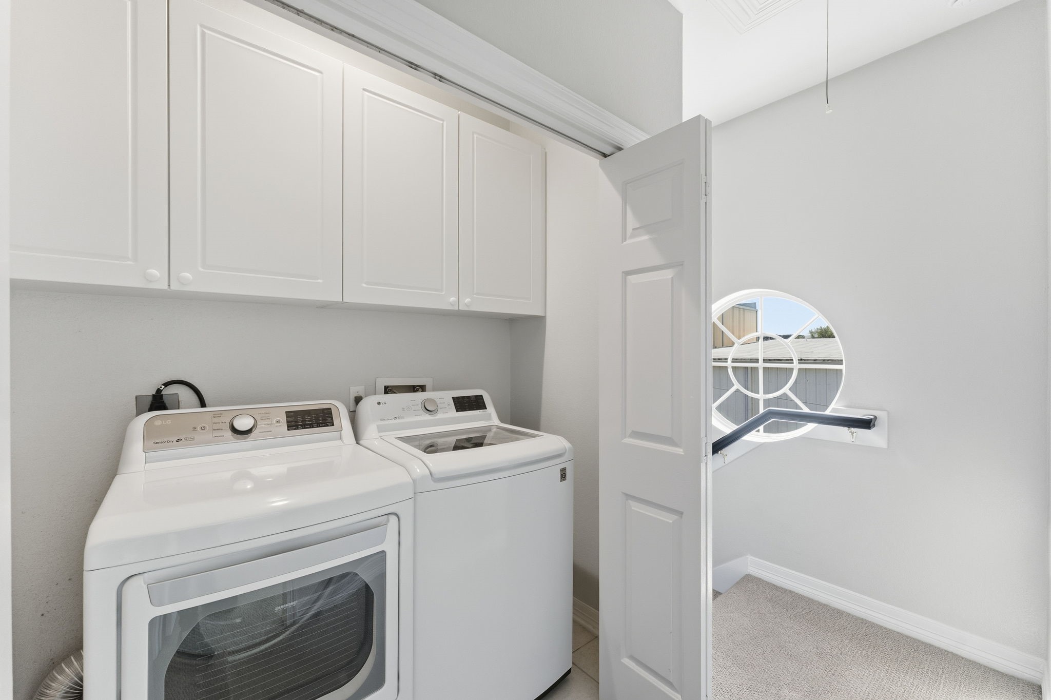 827 Rosine Street Houston, TX 77019 - Photo 34 of 50 This photo shows a compact laundry room with a washer and dryer, white cabinetry for storage, and a window providing natural light. Perfect for efficient laundry handling.
