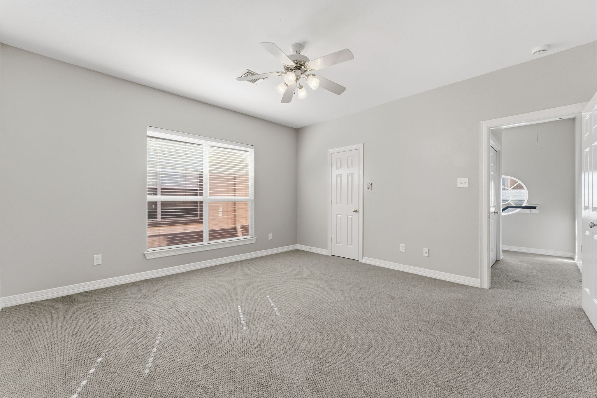 827 Rosine Street Houston, TX 77019 - Photo 46 of 50 This spacious, bright bedroom features neutral gray walls, plush carpeting, a ceiling fan, and ample natural light from a large window. It includes a closet and connects to another room, providing versatile living space.