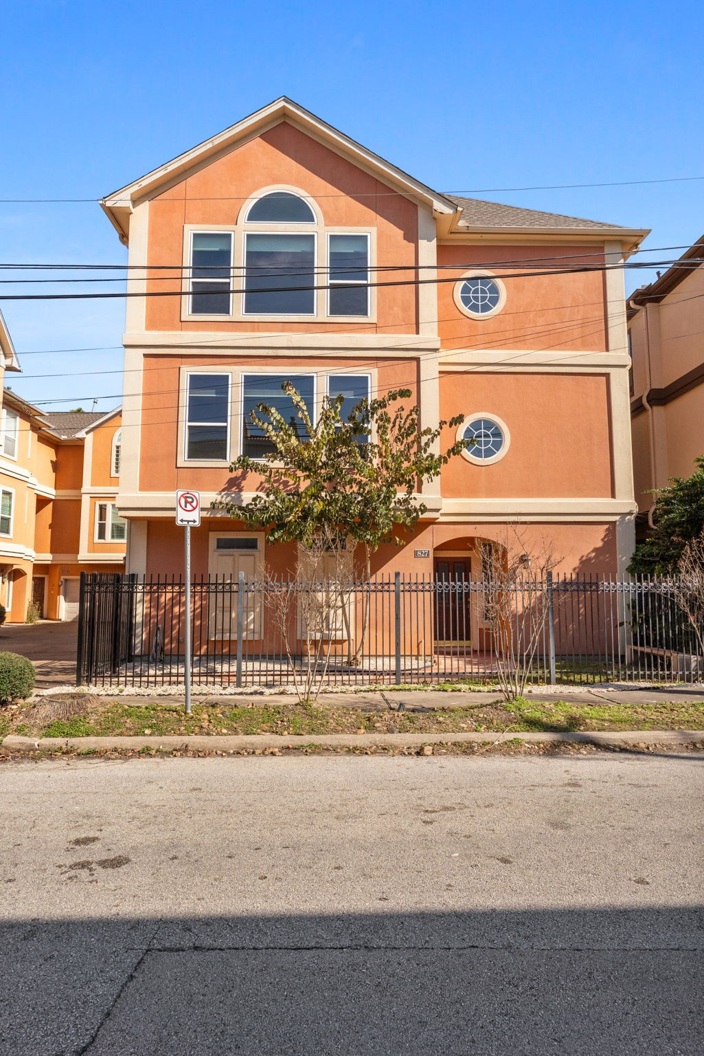 827 Rosine Street Houston, TX 77019 - Photo 6 of 50 This home is a three-story, peach-colored building featuring large windows and a circular accent window. It has a gated front yard with minimal landscaping and is located on a quiet street.