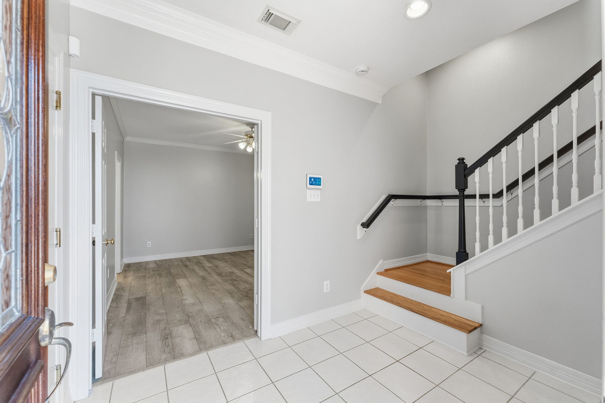 827 Rosine Street Houston, TX 77019 - Photo 9 of 50 Bright entryway with tiled flooring leads to a room with wood-style floors. A staircase with a dark handrail and white spindles adds a classic touch. Neutral gray walls and recessed lighting create a welcoming atmosphere.