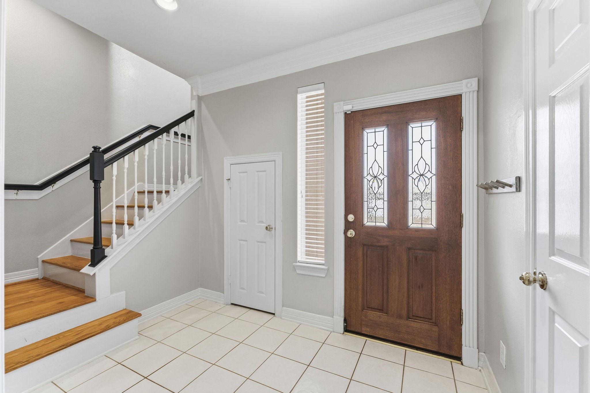 827 Rosine Street Houston, TX 77019 - Photo 10 of 50 This entryway features a wooden front door with decorative glass panels, a staircase with wooden steps and white railing, and a small storage closet under the stairs. The space is bright with tiled flooring and a neutral color palette.