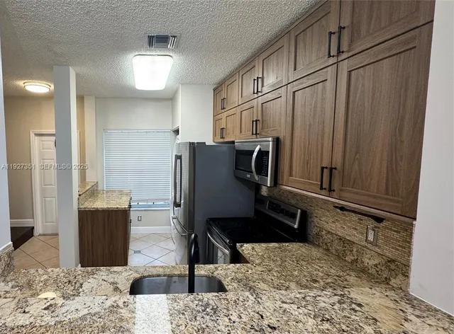 a living room with stainless steel appliances kitchen island granite countertop a refrigerator and a wooden cabinets